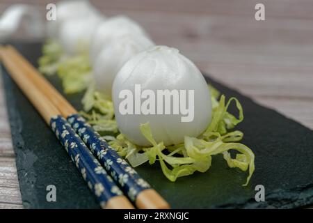 Xiao long Bao de crevettes sur un lit de laitue sur une assiette d'ardoise avec des baguettes et une cuillère en céramique avec de la sauce soja Banque D'Images