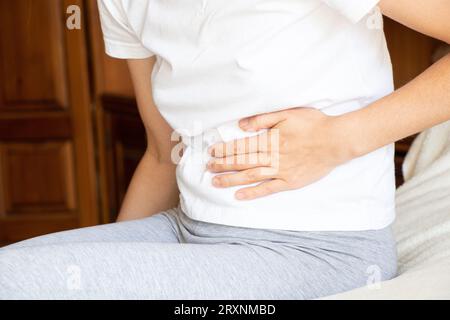 Une fille est assise sur le lit avec un estomac douloureux et tient son estomac, douleur aiguë dans l'abdomen, malade Banque D'Images