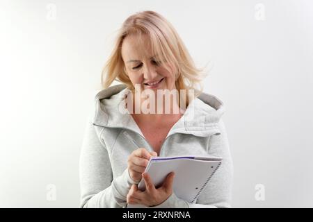 faire des plans pour l'avenir écrire dans un cahier avec un stylo, une femme blonde adulte sur un fond blanc écrit des idées de plans pour le jour de l'achat, des décisions de penser. levez la tête Banque D'Images