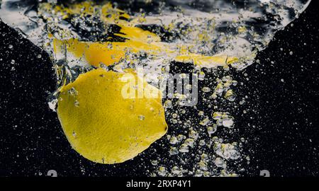 Sous l'eau de limonade sucrée fraîchement pressée que les citrons crus tranchent tombant dans l'eau de soude sur fond bleu foncé ou noir. Gros plan lemonad Banque D'Images