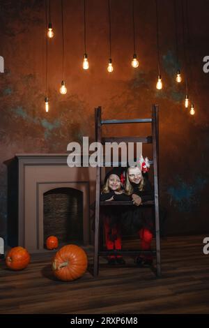 Des petites sorcières se tiennent appuyées sur les escaliers, souriantes. Il y a des citrouilles à proximité et des lanternes brûlent en arrière-plan. Halloween. Banque D'Images