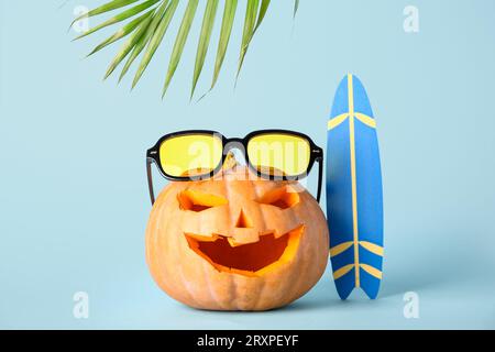 Citrouille sculptée pour Halloween avec des lunettes de soleil élégantes et planche de surf sur fond bleu Banque D'Images