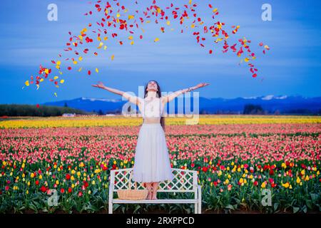 Femme debout sur un banc jetant des pétales de tulipes dans l'air Banque D'Images
