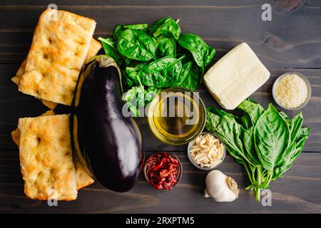 Ingrédients du sandwich végétarien grillé italien sur une table en bois : aubergines fraîches, basilic, pain focaccia et autres ingrédients du sandwich méditerranéen Banque D'Images