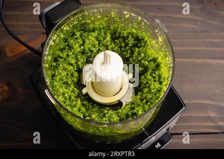 Pesto fraîchement mélangé dans un petit robot culinaire : ingrédients de sauce pesto italienne comprenant le basilic et l'huile d'olive mélangés dans une mini-préparation Banque D'Images