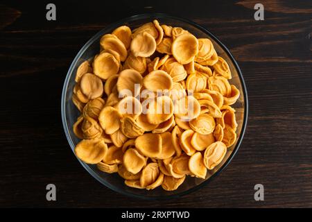 Pâtes à l'orecchiette à l'orange séchées dans un bol en verre : un bol de pâtes à l'orecchiette non cuites sur une table en bois vue du dessus Banque D'Images