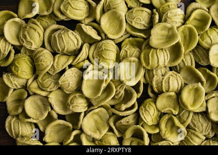 Pâtes orecchiette vertes séchées écaillées sur une table en bois : morceaux de pâtes orecchiette non cuites sur un fond de bois sombre Banque D'Images