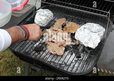 Steak de bœuf sur un grill cuit au charbon de bois et quelques pommes de terre farcies enveloppées dans de l'aluminium dans un après-midi de convivialité avec des amis en famille en plein air Banque D'Images