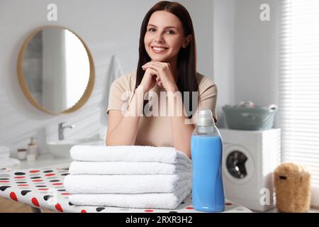Femme près de l'adoucisseur de tissu et serviettes propres dans la salle de bain Banque D'Images