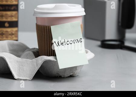 Note autocollante avec le mot Welcome attaché à la tasse de papier de café sur le bureau Banque D'Images