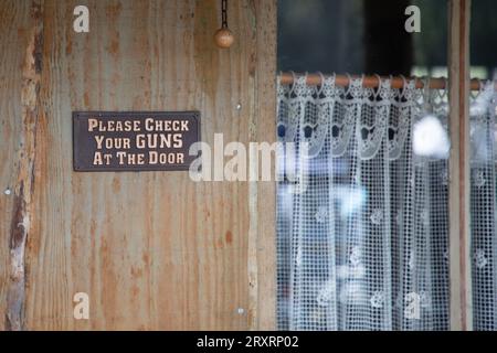 S'il vous plaît vérifier vos armes à la porte panneau signe métallique de texte dans la barre en bois l'entrée de façade saloon signifie armes interdites Banque D'Images