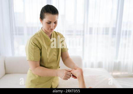 Portrait moyen de masseur féminin faisant des exercices orthopédiques de jambe de l'adolescente fille cliente, pétrissant sa cheville, prévention de la douleur dans le pied. Banque D'Images