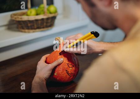 La citrouille Halloween de Jack. Les mains de l'homme sculptent la bouche avec un couteau en papier. Image avec mise au point sélective Banque D'Images