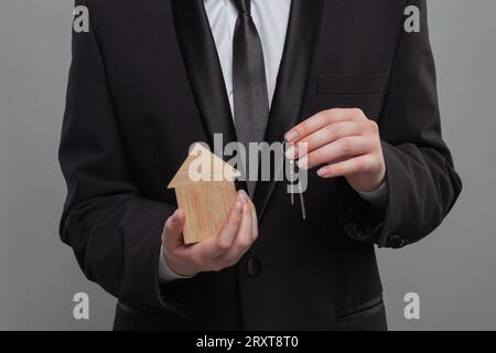 Gros plan de la main tenant les clés et la maison en bois sur fond gris Banque D'Images