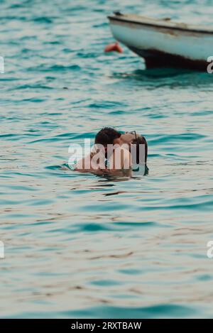 Un jeune couple romantique partageant un baiser passionné au milieu de la beauté sereine de l'océan au coucher du soleil. Banque D'Images