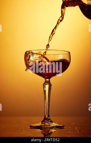 Gros plan photo de verser du whisky, du rhum, du brandy ou du gin de la bouteille en verre haut sur fond dégradé doré. Banque D'Images