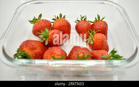 Un plat en verre transparent contenant des fraises rouges juteuses photographiées sur fond blanc. Banque D'Images