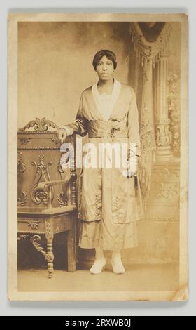 Carte postale photographique d'une femme debout à côté d'une chaise en bois 1904-1918 Banque D'Images