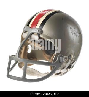 Un casque de football Ohio State Buckeyes porté par Archie Griffin. Le casque en plastique dur est gris avec des lignes noires, blanches et rouges allant verticalement de l'avant vers l'arrière au milieu du casque. Il y a des trous sur toute la surface du casque. L'intérieur du casque a un rembourrage noir épais. Les barres métalliques grises recouvertes de plastique forment un masque facial. Le masque facial dépasse sévèrement de l'avant du casque. Il a une barre verticale au centre et deux barres horizontales incurvées avec des barres supplémentaires entre les barres horizontales en trois sections. Il y a une mentonnière en cuir blanc, sna Banque D'Images