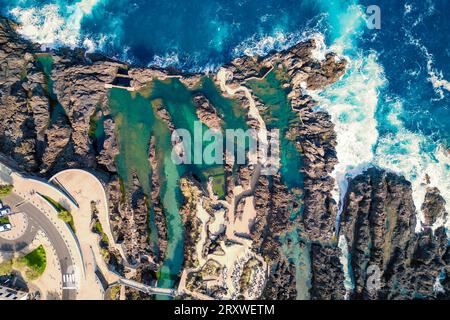 Fantastique, vue panoramique des gens nageant dans les piscines de lave naturelle à Porto Moniz, Madère, Portugal, tandis que la mer fait rage autour d'eux Banque D'Images