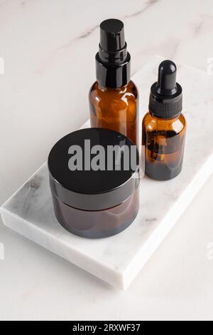 Trois maquettes de produits cosmétiques sur podiums de marbre. Contexte pour la présentation de cosmétique. Flacons en verre ambré avec couvercles noirs Banque D'Images