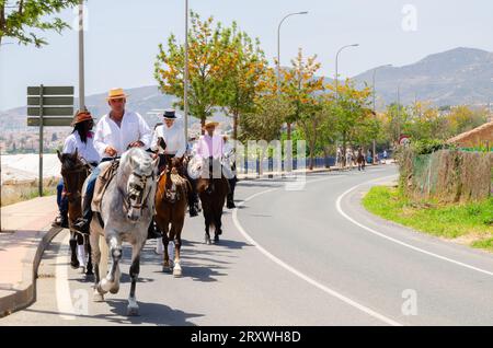 NERJA, ESPAGNE - 15 MAI 2022 femmes en robes flamenco et hommes sur des chevaux andalous vêtus de leurs meilleurs costumes folkloriques traditionnels et chapeau à large bord Banque D'Images