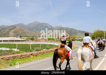 NERJA, ESPAGNE - 15 MAI 2022 femmes en robes flamenco et hommes sur des chevaux andalous vêtus de leurs meilleurs costumes folkloriques traditionnels et chapeau à large bord Banque D'Images