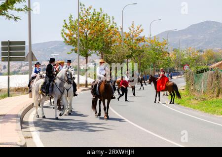 NERJA, ESPAGNE - 15 MAI 2022 femmes en robes flamenco et hommes sur des chevaux andalous vêtus de leurs meilleurs costumes folkloriques traditionnels et chapeau à large bord Banque D'Images