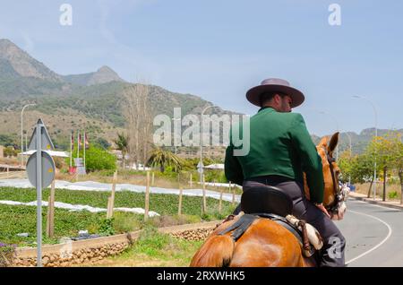 NERJA, ESPAGNE - 15 MAI 2022 femmes en robes flamenco et hommes sur des chevaux andalous vêtus de leurs meilleurs costumes folkloriques traditionnels et chapeau à large bord Banque D'Images