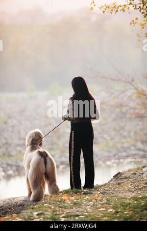 Femme et chien regardant l'horizon près d'une rivière dans les bois d'automne Banque D'Images