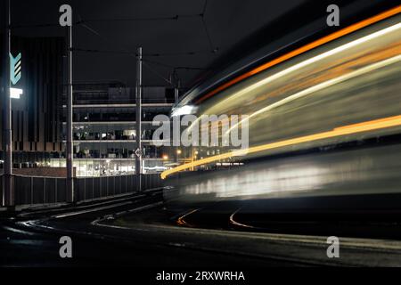 Mouvement flou des tramways circulant sur les rails à Nottingham City la nuit avec des sentiers de tramway légers et des bâtiments urbains éclairés en arrière-plan Banque D'Images