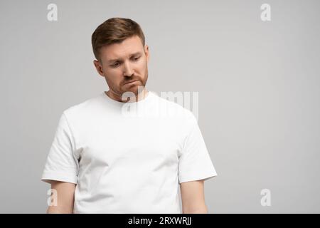 Triste homme déçu avec la tête vers le bas sur fond gris. Portrait de jeune homme frustré contrarié. Banque D'Images