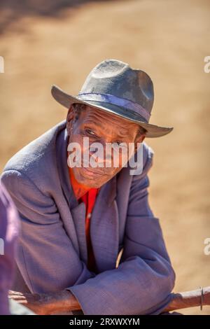 vieil homme africain dans le village, portant un chapeau, situé sur la chaise dans sa cour Banque D'Images