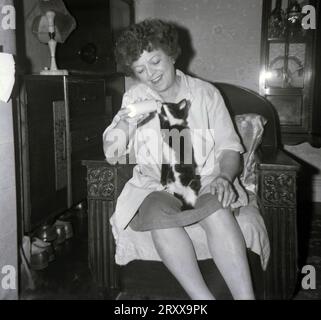 1960, historique, assise dans un fauteuil dans une chambre avant, une dame donnant du lait à son chaton à partir d'une petite bouteille en plastique, Angleterre, Royaume-Uni. Banque D'Images