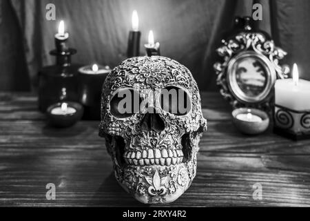Nature morte noire et blanche avec crâne décoré sur une table en bois, bougies allumées et toile de fond Banque D'Images