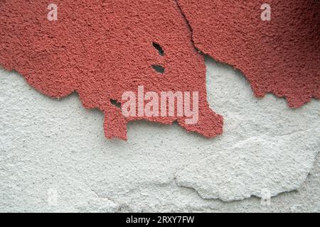 Une peinture texturée rouge se détache d'un mur de plâtre blanc Banque D'Images