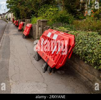Barrières de construction en plastique rouge empilées le long d'un trottoir résidentiel à côté de murs de pierre et de végétation envahie Banque D'Images