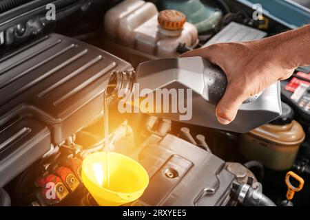 Un mécanicien de sexe masculin verse de l'huile moteur de la cartouche dans le moteur de la voiture Banque D'Images