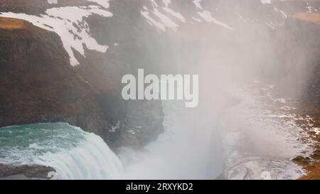 Cascade Gullfoss à reykjavik vers mars 2023 avec un débit d'eau spectaculaire et des paysages islandais. Majestueuse cascade de rivière près des falaises enneigées gelées et des champs, vue panoramique. Banque D'Images