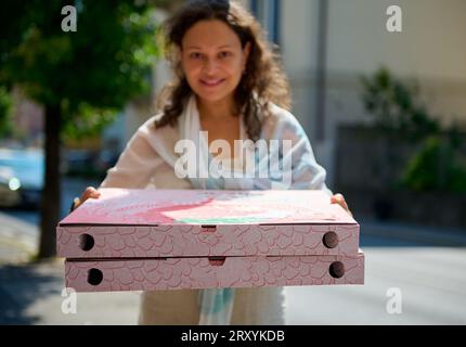Gros plan de deux grandes boîtes en carton jetables avec une pizza napolitaine fraîchement cuite à emporter, dans les mains d'une jolie femme floue souriante et regardant Banque D'Images