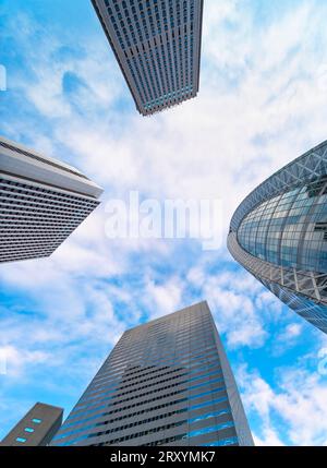 Vue vertigineuse à faible angle des gratte-ciel sous un ciel bleu avec les façades vitrées des bâtiments emblématiques de Shinjuku tels que l'école HAL en forme de cocon Banque D'Images