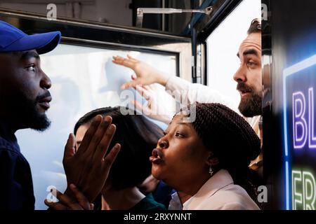 Un agent de sécurité afro-américain apaisant frénétique et anxieux, divers acheteurs s'introduisent dans un centre commercial pendant le Black Friday. Agent de police gérant la foule et réduisant la violence Banque D'Images