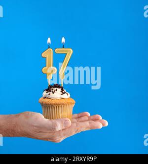 Main livrant cupcake d'anniversaire - bougie numéro 17 sur fond bleu Banque D'Images