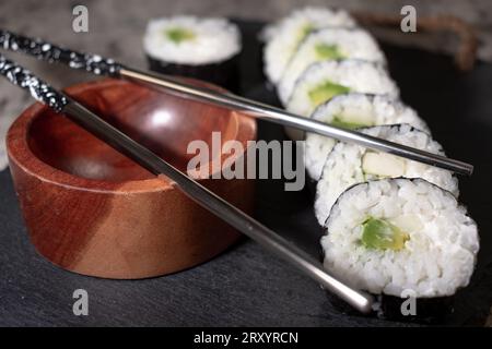 Sushi végétarien fait maison avec algues, riz, concombre, avocat et fromage végétalien. A côté, un récipient en bois pour sauce soja et méta réutilisable Banque D'Images