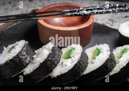 Sushi végétarien fait maison avec algues, riz, concombre, avocat et fromage végétalien. A côté, un récipient en bois pour sauce soja et méta réutilisable Banque D'Images