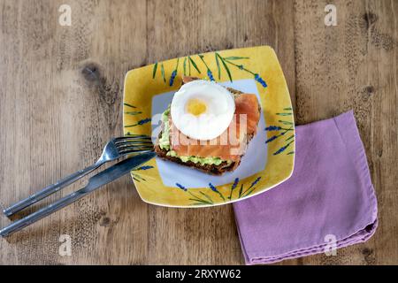 Pain grillé avec purée d'avocat, saumon fumé et œuf poché sur une table en bois Banque D'Images