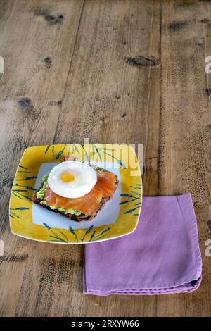 Pain grillé avec purée d'avocat, saumon fumé et œuf poché sur une table en bois Banque D'Images