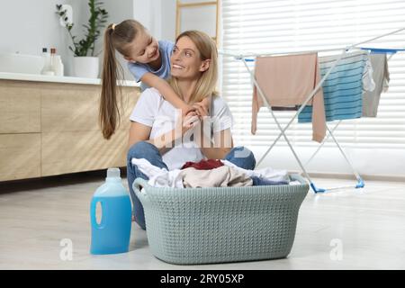 Mère et fille assis sur le sol près du panier avec des vêtements sales et assouplissant dans la salle de bains Banque D'Images