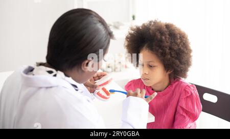 Dentiste afro-américain expliquant à un enfant afro métis comment se brosser les dents. Le médecin et le concept de santé de l'enfant. Banque D'Images