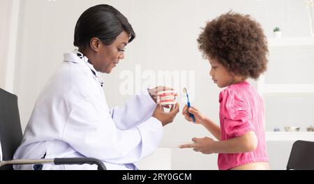 Dentiste afro-américain expliquant à un enfant afro métis comment se brosser les dents. Le médecin et le concept de santé de l'enfant. Banque D'Images